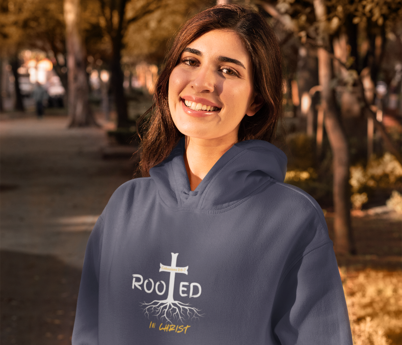 Woman wearing a blue hoodie with a cross and roots design, standing outdoors.